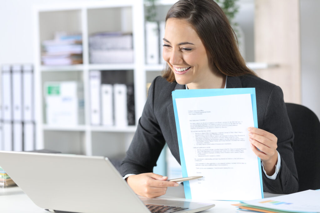 woman smiling holding paper and pen in front of laptop
